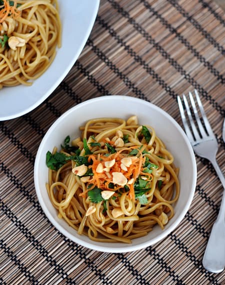 Top view of a white bowl of cooked thai noodles topped with herbs and chopped peanuts.