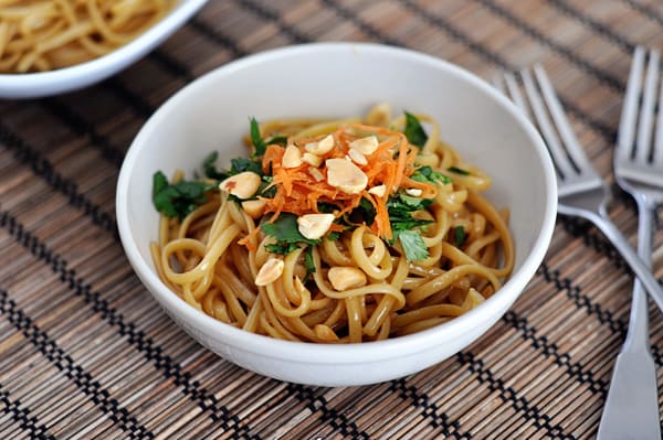 White bowl with cooked thai linguine noodles topped with herbs and peanuts.