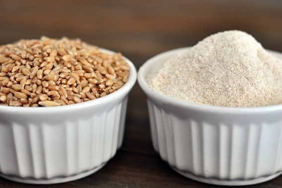 two bowls side by side with one full of wheat kernels and one full of ground wheat