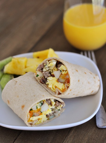 A breakfast burrito cut in half on a white plate next to fresh fruit.