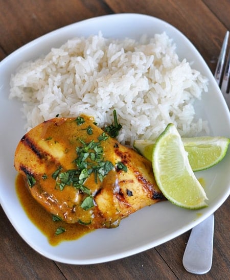 Top view of a white plate with grilled chicken, white rice, and lime slices.