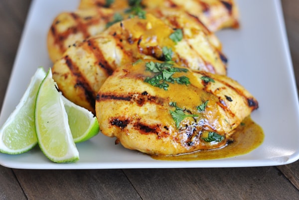 A white platter of grilled chicken with lime slices on the side.