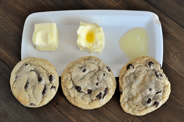 Top view of three chocolate chip cookies with butter in different states of being melted behind the cookies.