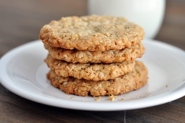 Four thin and crispy oatmeal cookies stacked on top of each other on a white plate.