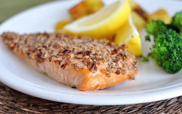 Pecan-crusted salmon on a white plate with lemon slices and broccoli.