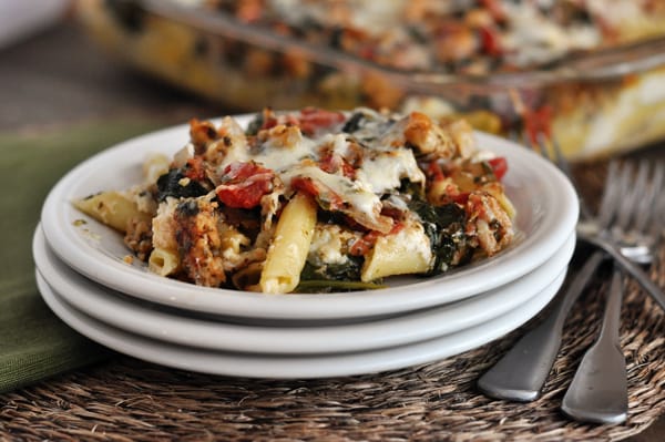 A big helping of pesto sausage baked ziti on the top plate of three stacked white plates.