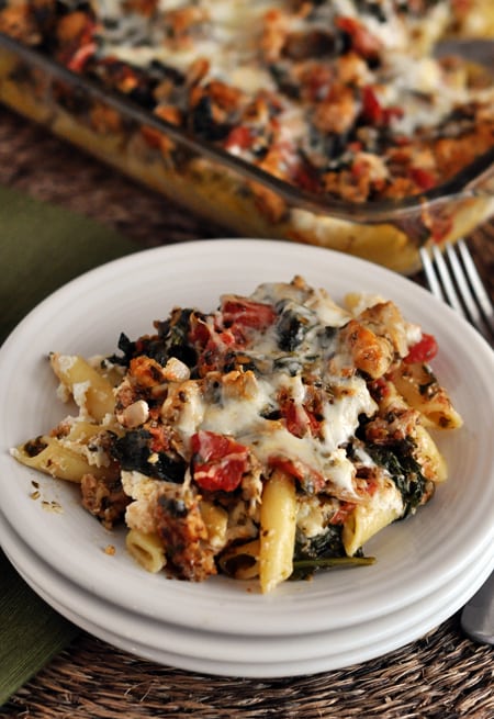A big helping of pesto and sausage baked ziti on a white plate.