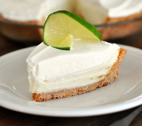A slice of sour cream lime tart on a white plate, with a slice of lime on top.