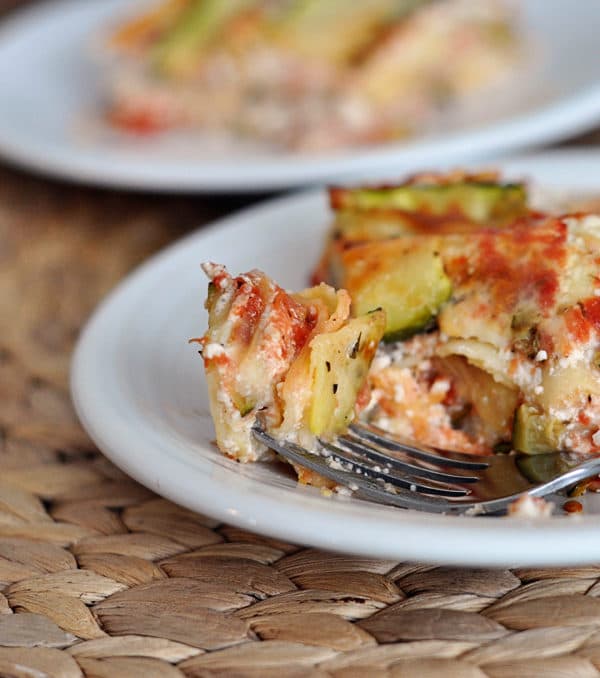 A white plate with a cheesy zucchini lasagna with a fork taking a bite out.