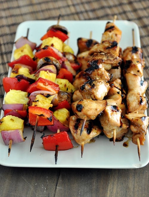 Top view of a white platter with grilled chicken and veggie kebabs.