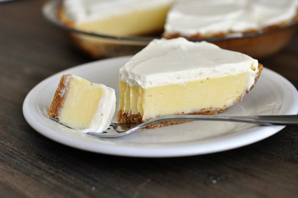 A slice of cream-topped lemon pie with one bite taken off on a fork.