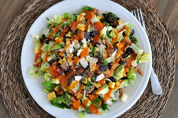 Top view of a white plate of taco salad with dressing drizzled on top.