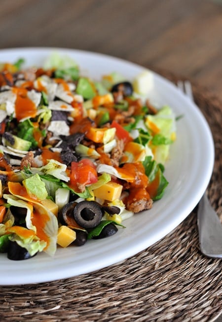 White plate full of taco salad with all the fixings and catalina dressing drizzled on top.