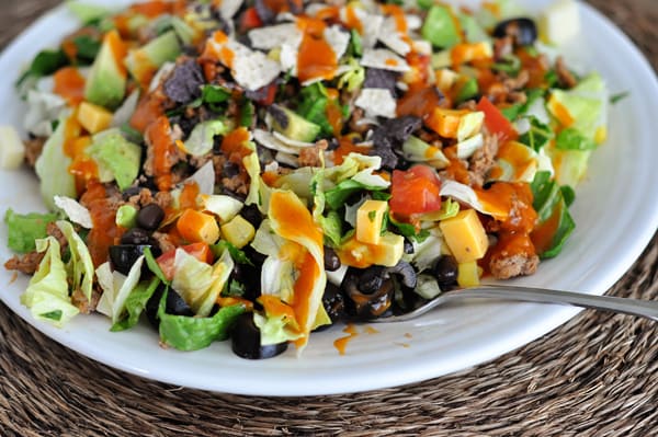 A white plate full of chopped taco salad and catalina dressing drizzeled on top.