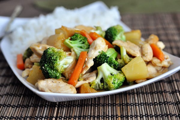 Chicken stir fry next to cooked white rice on a white platter.