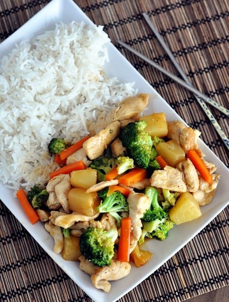 A white rectangular platter with cooked white rice on one side and chicken stir fry on the other.