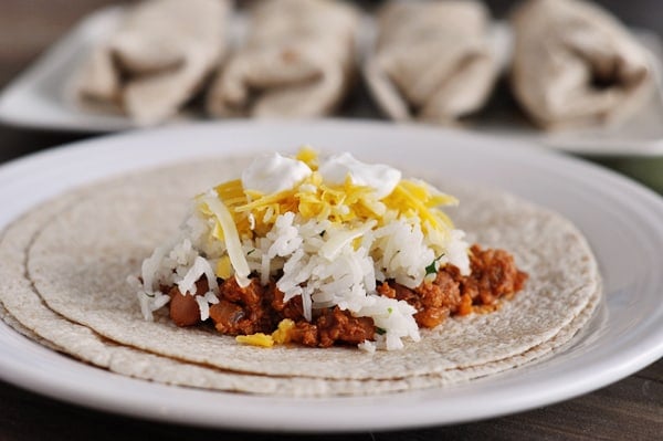 A tortilla with beef, beans, white rice, cheese, and sour cream on it.