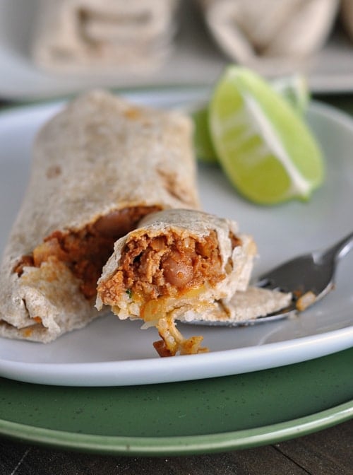 A fork cutting a bite out of a beef and bean burrito on a white plate.