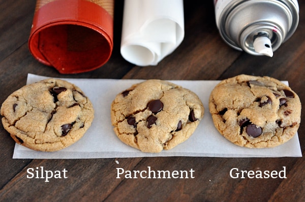 three chocolate chip cookies lined up with the words silpat, parchment, and greased underneath