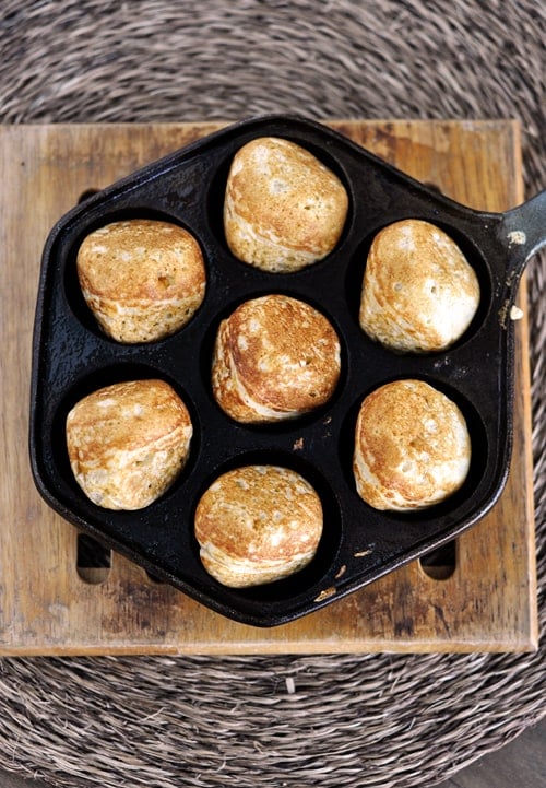 Top view of an ebelskiver pan with seven golden brown cooked ebelskivers in it.