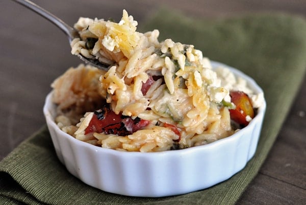 A small white ramekin filled with cooked cheesy orzo.