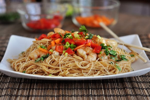 Cooked noodles topped with shrimp and diced vegetables on a white platter.