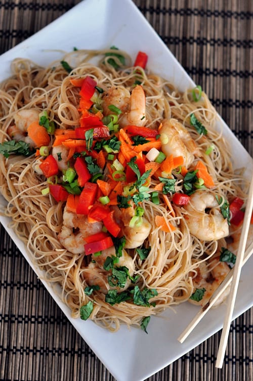 Top view of a rectangular white dish with cooked noodles topped with shrimp and chopped vegetables.