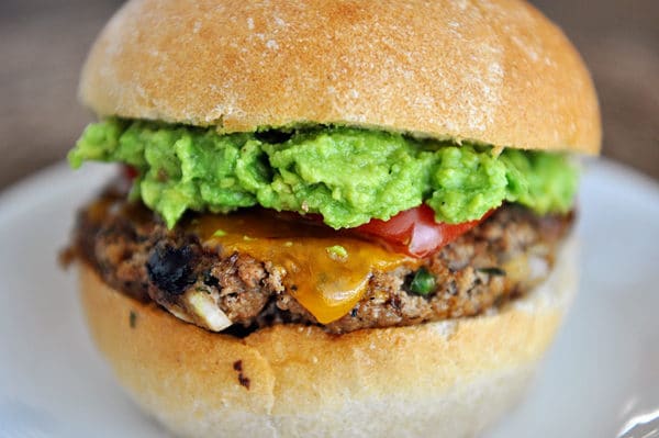 A jalapeno cheddar burger topped with guacamole and tomato slices on a white plate. 