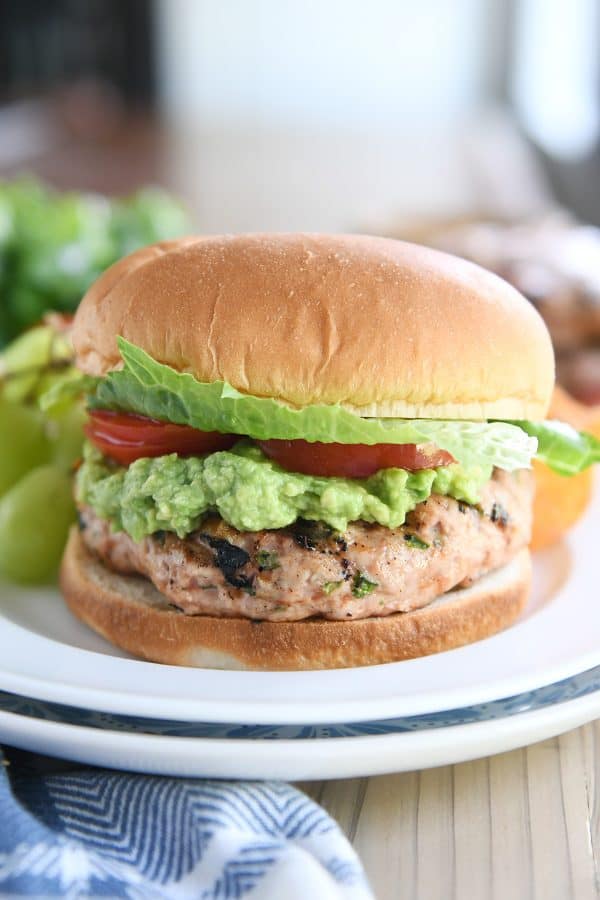 Jalapeno turkey burger with guacamole, tomato, and lettuce on a white plate.