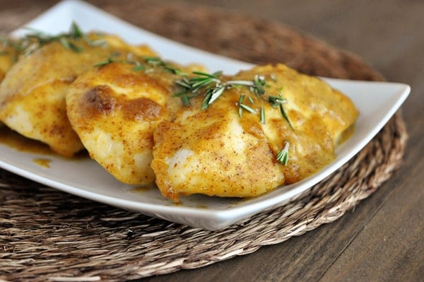 Cooked chicken breasts covered in a mustard sauce in a white platter.