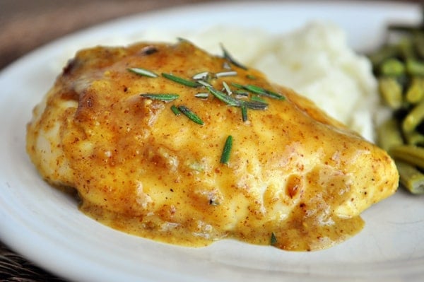 Mustard-sauce covered chicken breast on a white plate next to a helping of mashed potatoes and green beans.