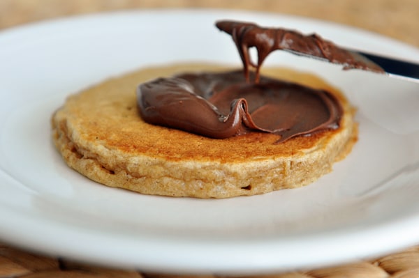 A pancake getting covered with Nutella.