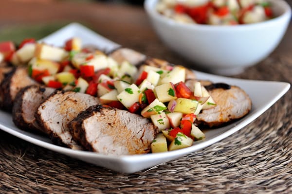 White platter with slices of grilled pork loin topped with fresh apple salsa.