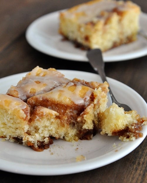 White plate with a piece of cinnamon roll cake with a bite taken out.