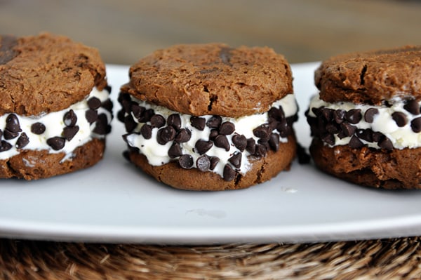 Three chocolate chip coated pumpkin ice cream sandwiches on a white plate.