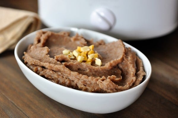 White oval dish full of refried beans in front of a slow cooker.