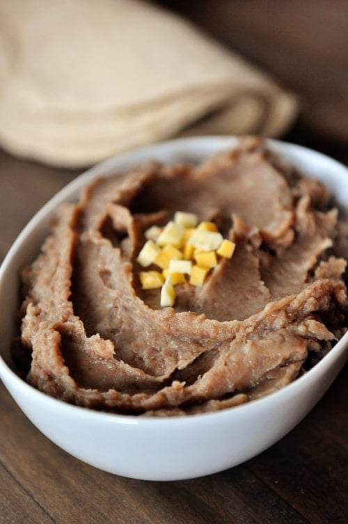 White oval dish full of refried beans topped with small cheese cubes.