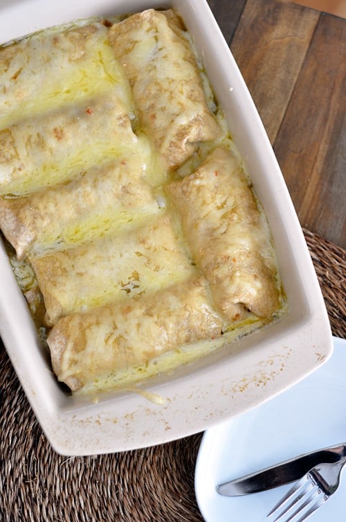 White ceramic 9x13 pan filled with cheesy, sauce-covered, cooked pork burritos.