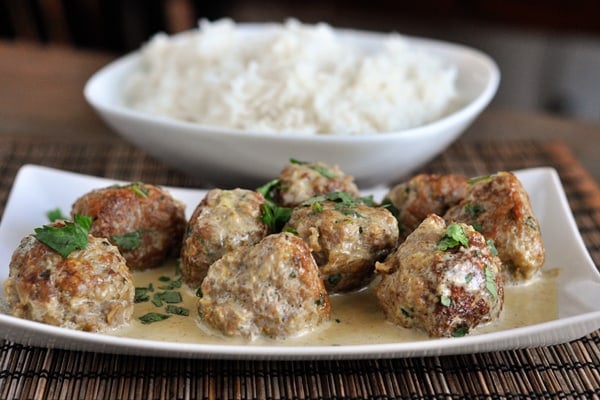 White dish with browned meatballs covered in sauce and parsley and a dish of cooked white rice behind it.