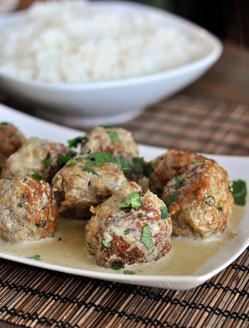 Curry sauce and parsley covered meatballs in a white dish.