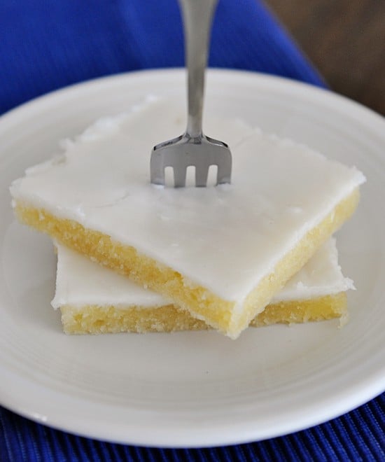 Two pieces of white Texas sheet cake stacked on top of each other with a fork stuck in the top piece.