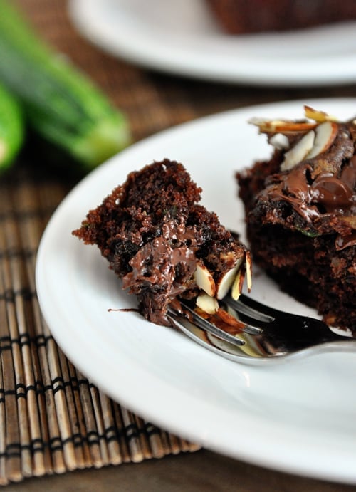 A chocolate cake with a bite taken out on a white plate.