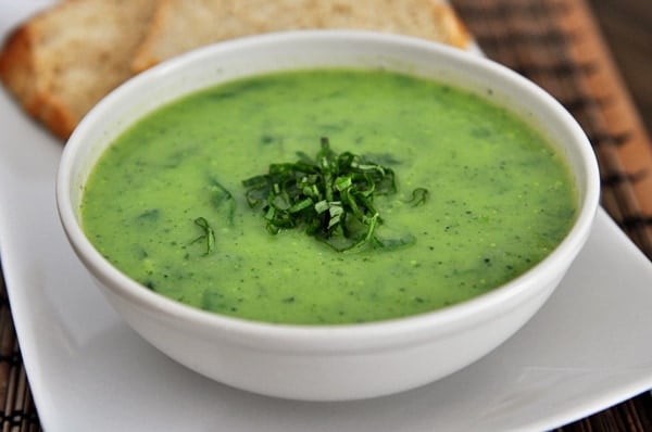 White bowl full of green soup topped with chopped chives.