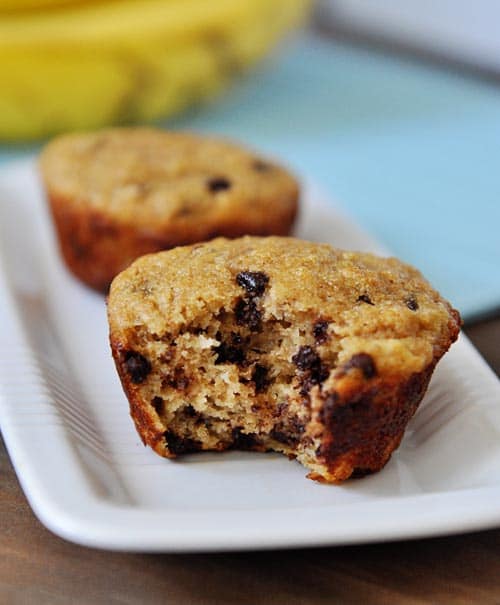 two banana chocolate chip muffins on a white plate, the front muffin has a bite out