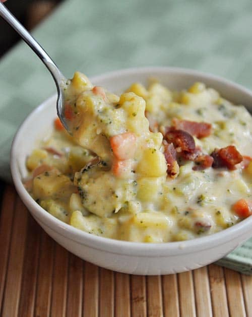 White bowl full of chunky broccoli cheese soup with a few small pieces of bacon on top.