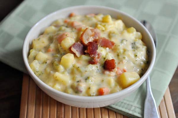 White bowl of broccoli cheese soup with a few bacon pieces on top.