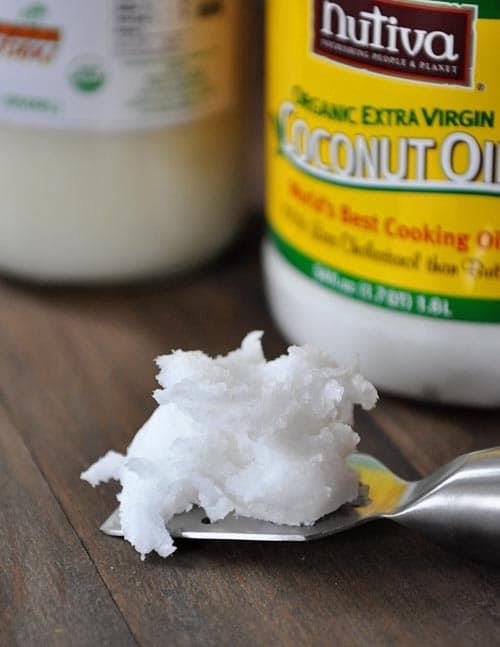 a scoop of coconut oil on a spatula in front of two jars of coconut oil