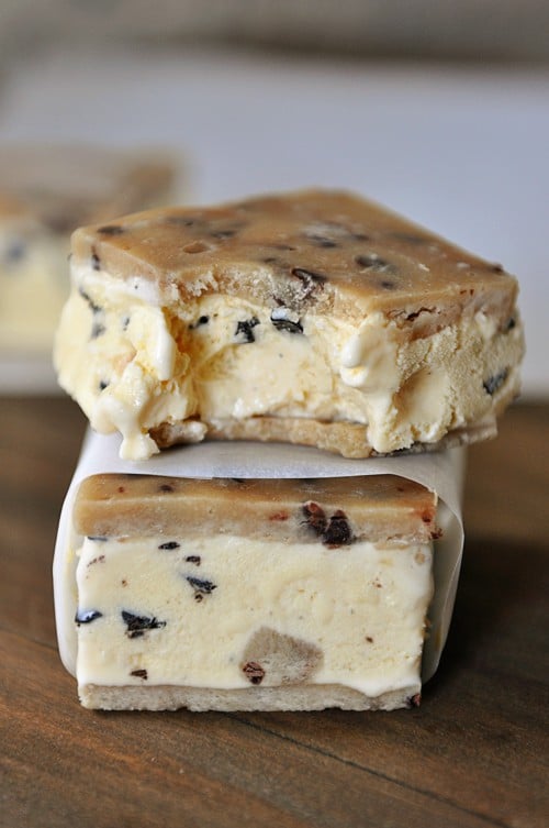 Two cookie dough ice cream sandwiches stacked on top of each other. The top one has a bite taken out. 