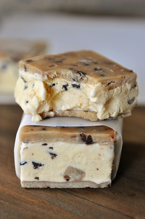 Two cookie dough ice cream sandwiches stacked on top of each other. The top one has a bite taken out.