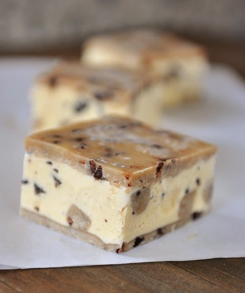 Three cookie-dough ice cream sandwiches lined up on a piece of parchment paper.